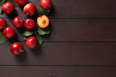 Photo of Delicious ripe cherry plums with leaves on wooden table, flat lay. Space for text
