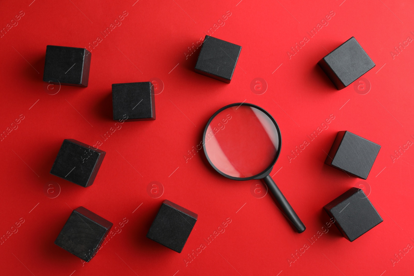 Photo of Black cubes and magnifier glass on red background, flat lay. Find keywords concept