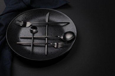 Stylish table setting. Plate, napkin and cutlery on black background, space for text