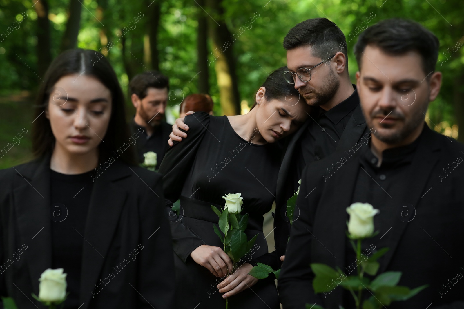 Photo of Funeral ceremony. Sad people with white rose flowers mourning outdoors