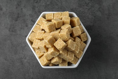 Photo of Brown sugar cubes in bowl on grey table, top view