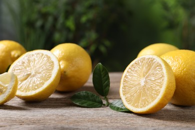 Photo of Fresh lemons and green leaves on wooden table outdoors, closeup