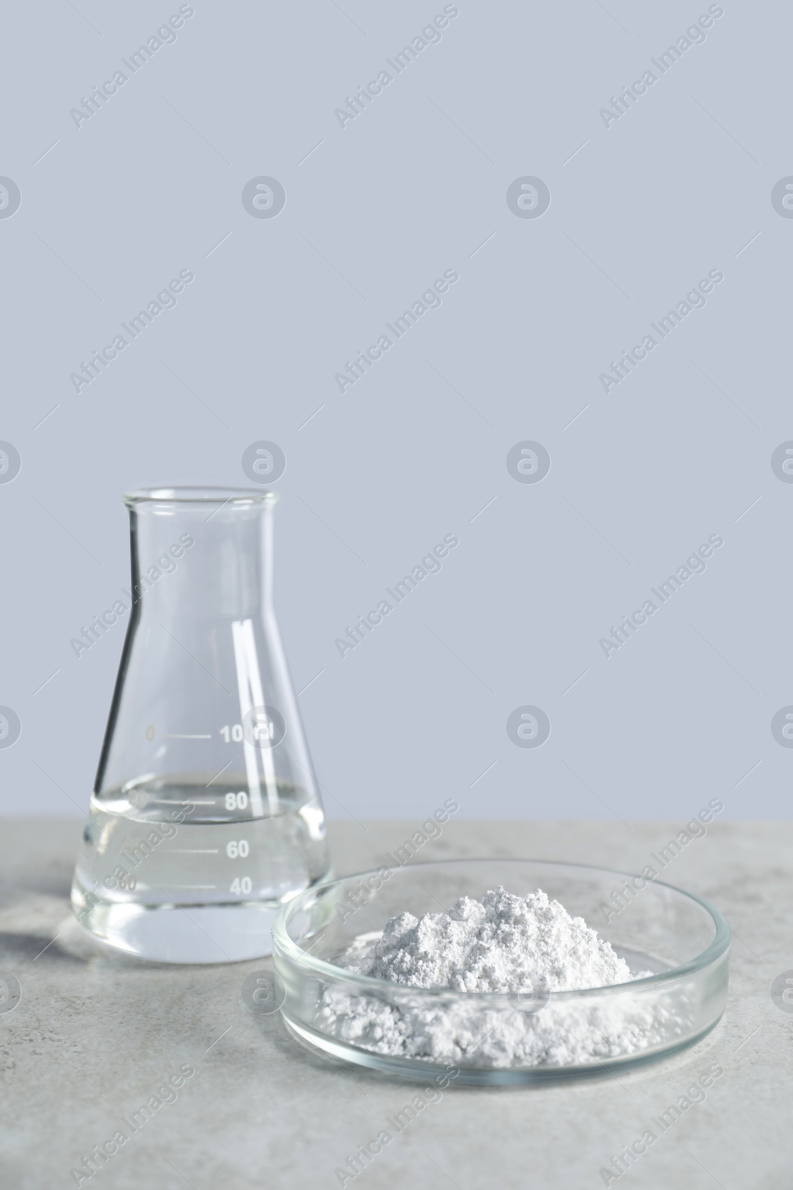 Photo of Petri dish with calcium carbonate powder and laboratory flask on light grey table