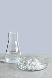 Petri dish with calcium carbonate powder and laboratory flask on light grey table