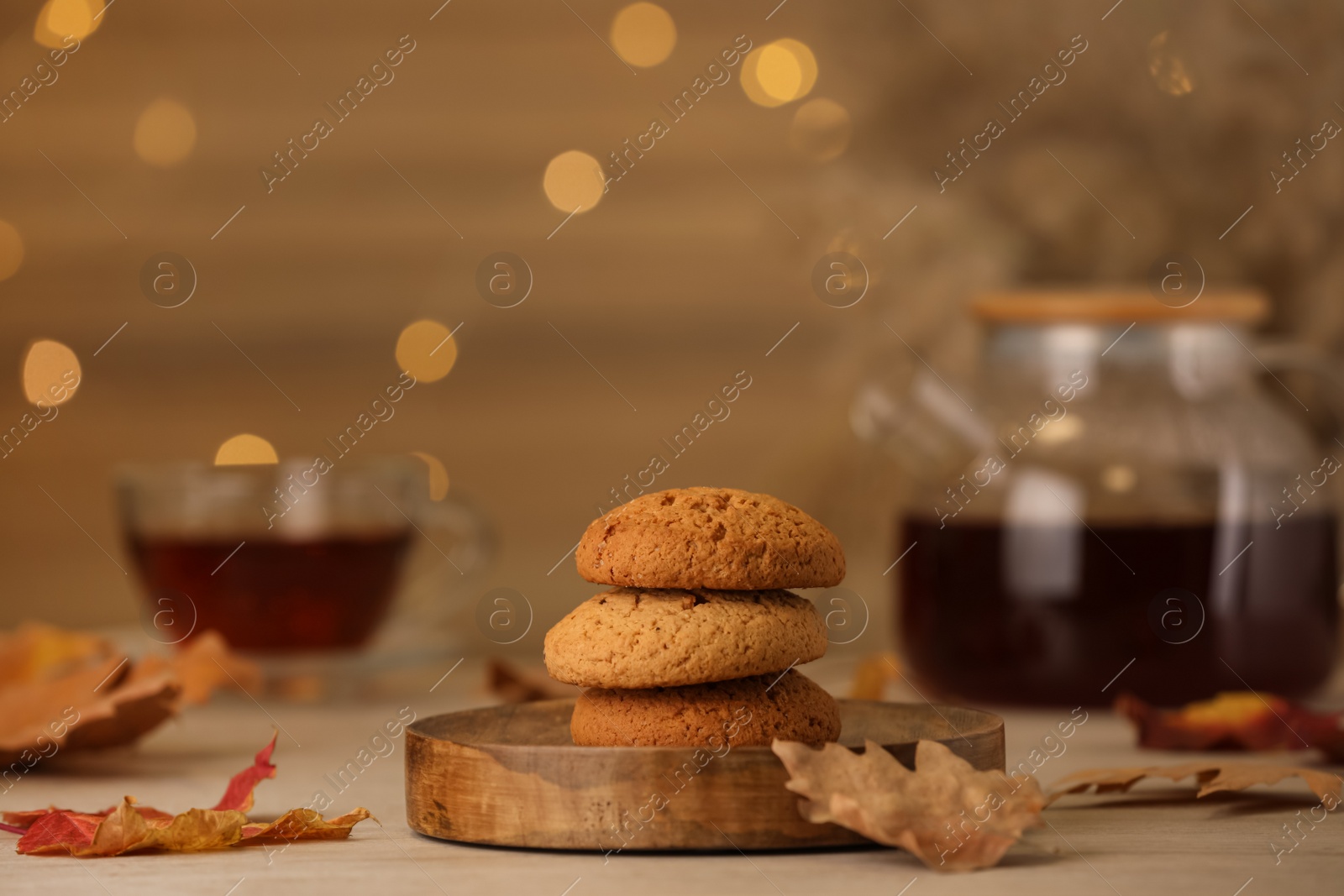 Photo of Delicious cookies and autumn leaves on wooden table against blurred lights