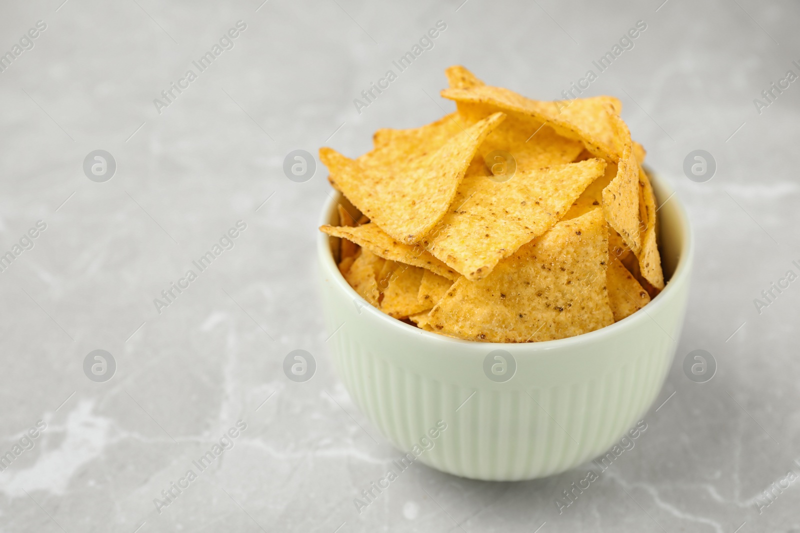 Photo of Bowl with tasty Mexican nachos chips on grey table, space for text