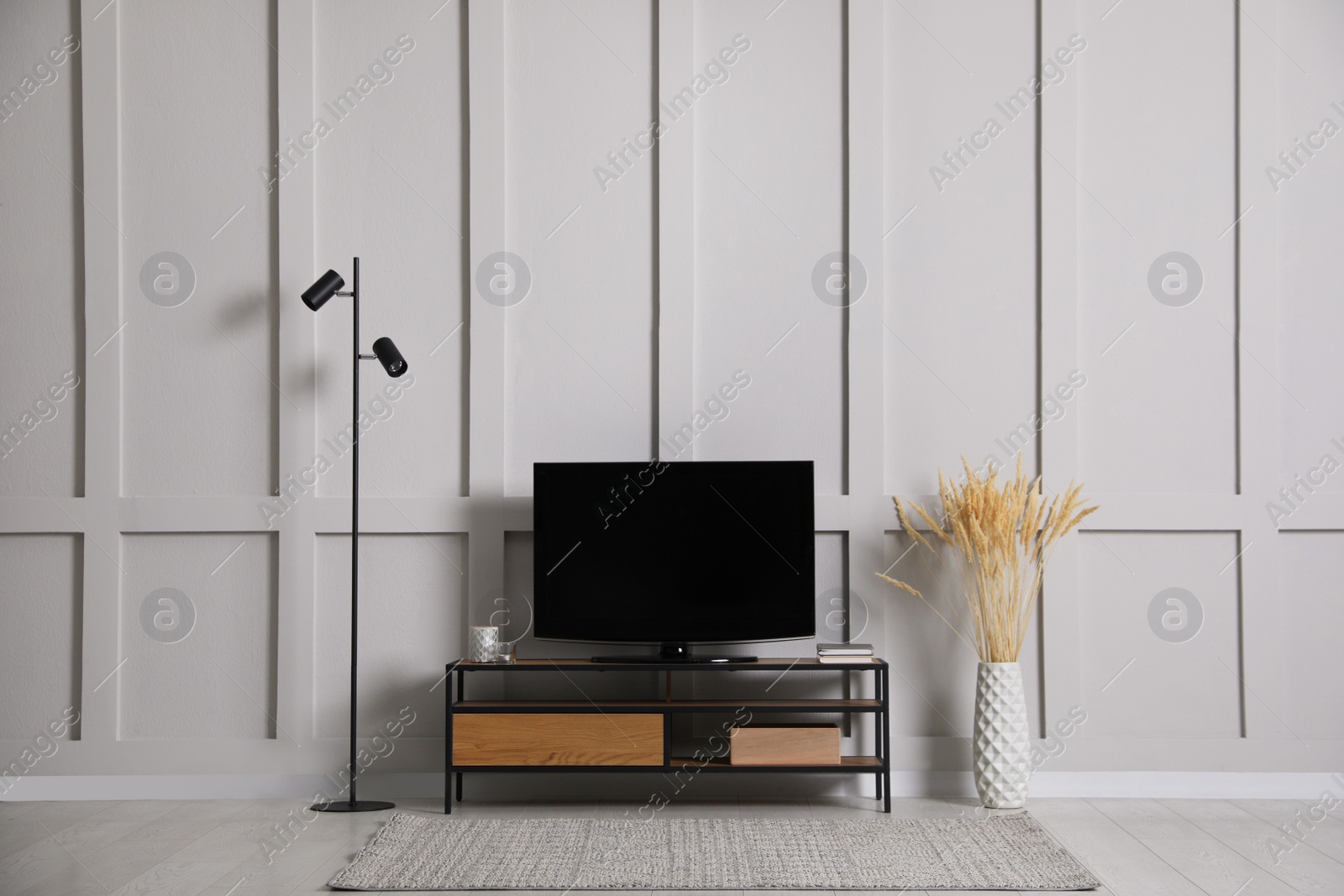 Photo of Elegant room interior with modern TV on stand, floor lamp and decorative dry plants