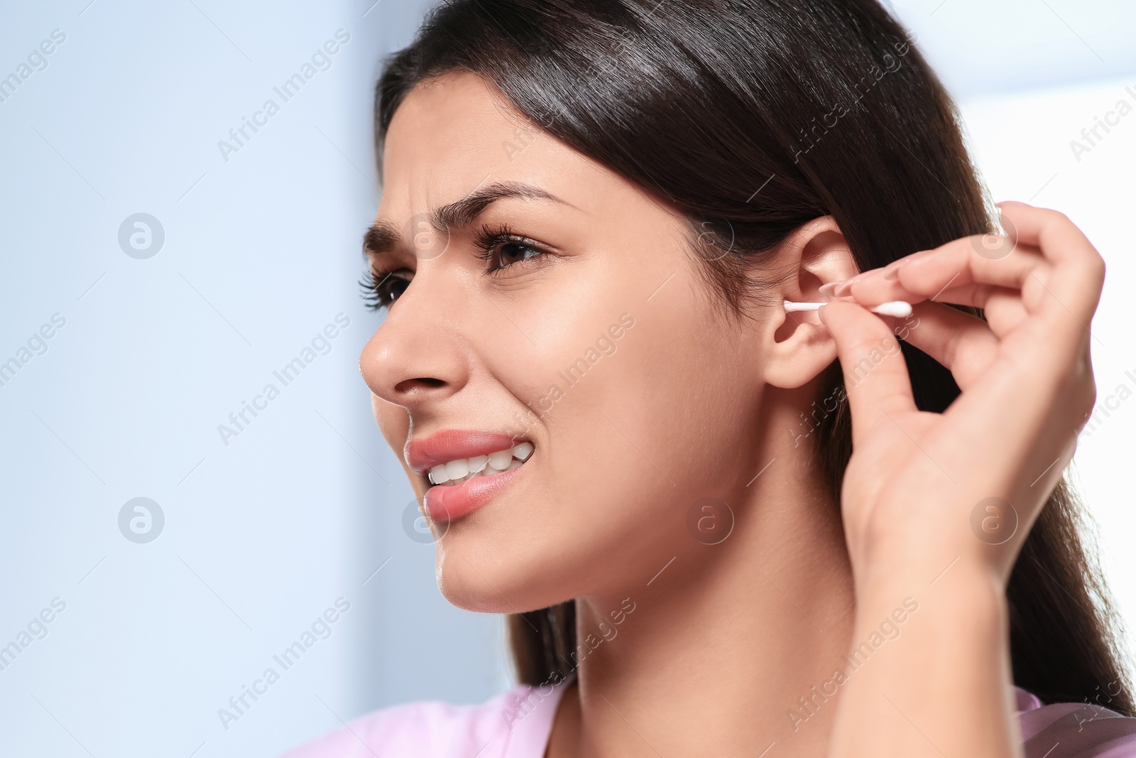 Photo of Young woman cleaning ear with cotton swab on blurred background, closeup