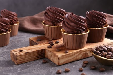 Photo of Delicious chocolate cupcakes and coffee beans on grey textured table, closeup