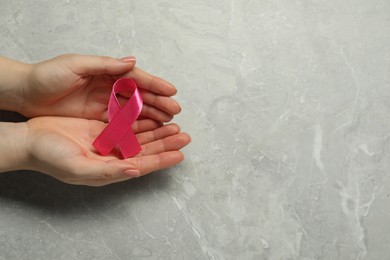 Photo of Breast cancer awareness. Woman with pink ribbon at grey marble table, top view. Space for text