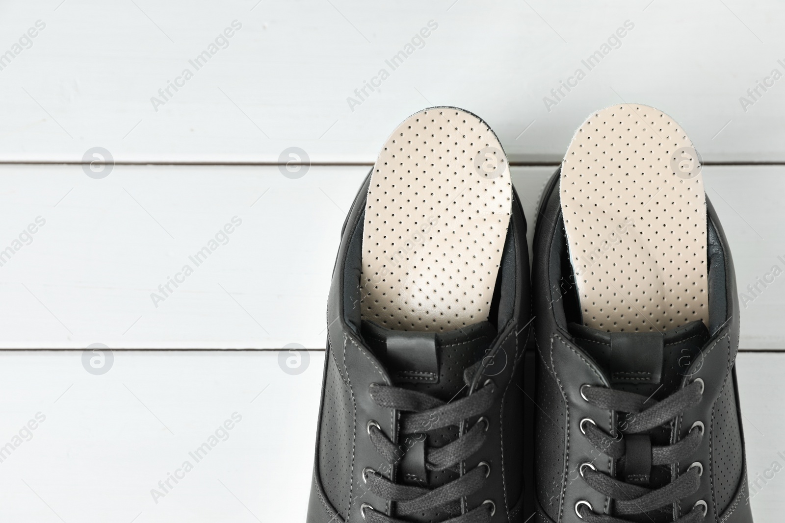 Photo of Orthopedic insoles in shoes on white wooden floor, flat lay. Space for text