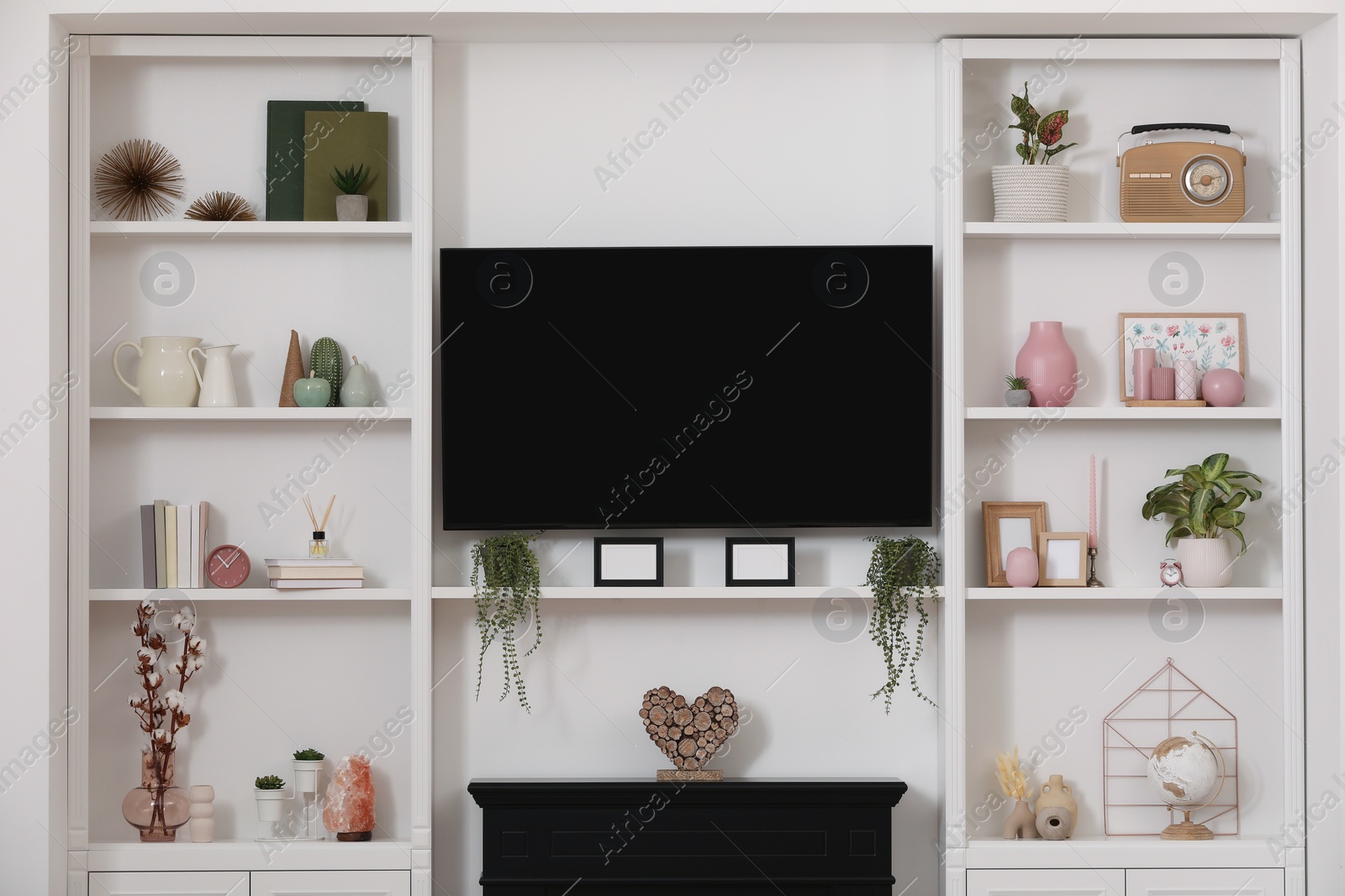 Photo of TV set, fireplace and stylish shelves with decorative elements and houseplants near white wall. Interior design