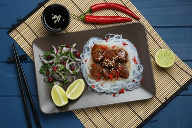 Photo of Pieces of soy sauce chicken with noodle, salad and lime served on blue wooden table, flat lay