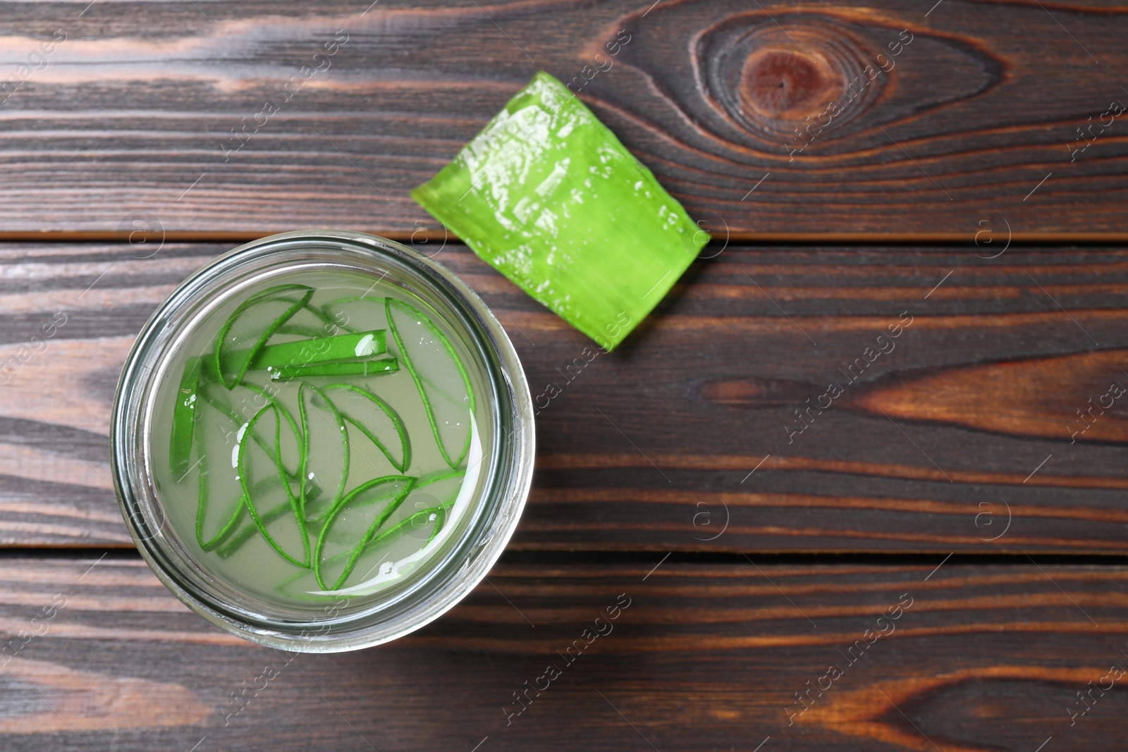 Photo of Fresh aloe juice in jar and leaf on wooden table, top view. Space for text