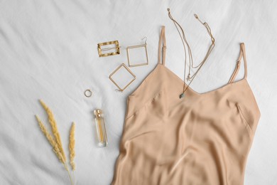 Stylish dress with golden bijouterie and perfume on white fabric flat lay