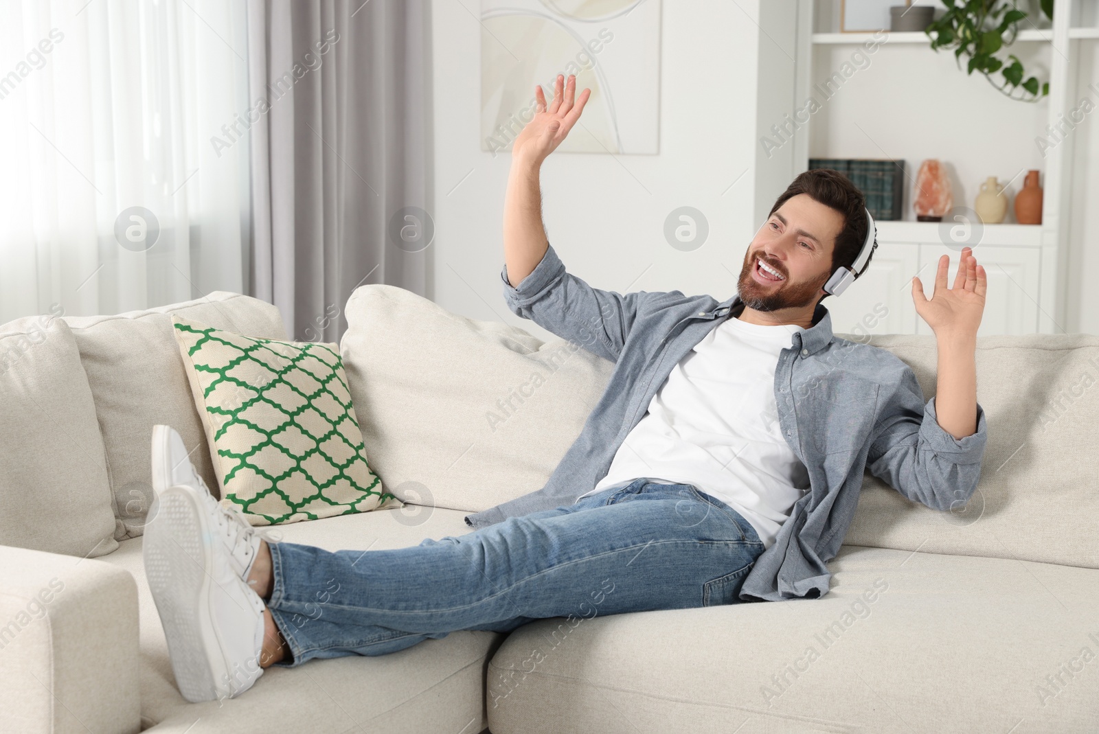 Photo of Happy man listening music with headphones on sofa indoors