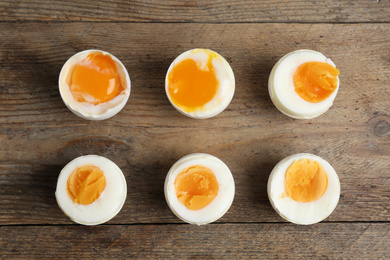 Photo of Different readiness stages of boiled chicken eggs on wooden table, flat lay