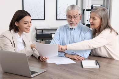 Photo of Elderly couple consulting insurance agent about pension plan at wooden table indoors