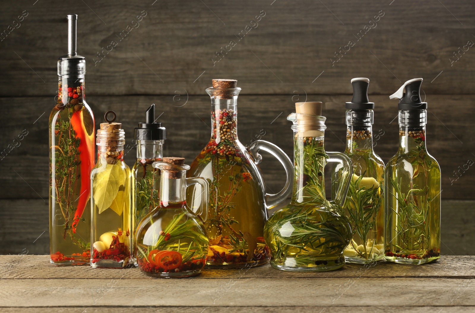 Photo of Cooking oil with different spices and herbs in bottles on wooden table