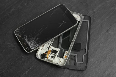 Photo of Parts of broken smartphone on black table, above view. Device repair