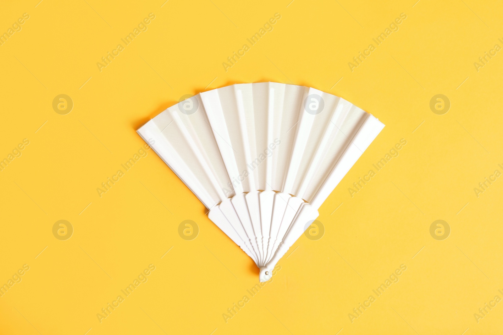 Photo of White hand fan on yellow background, top view