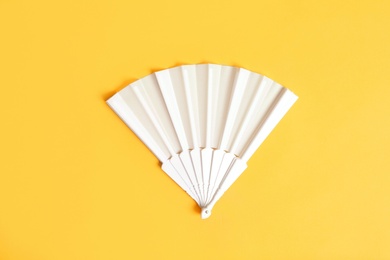 White hand fan on yellow background, top view