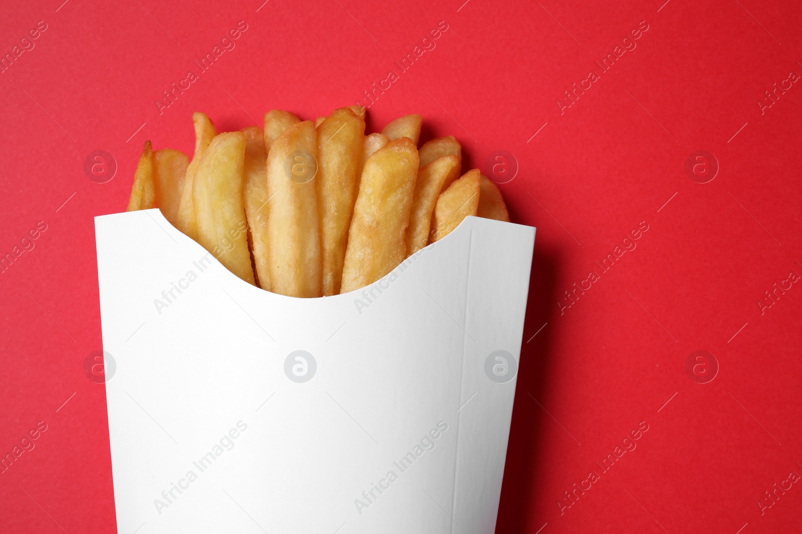 Photo of Paper cup with French fries on red table, top view. Space for text