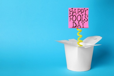 Photo of Lunch box with Happy Fools' Day note on light blue background. Space for text