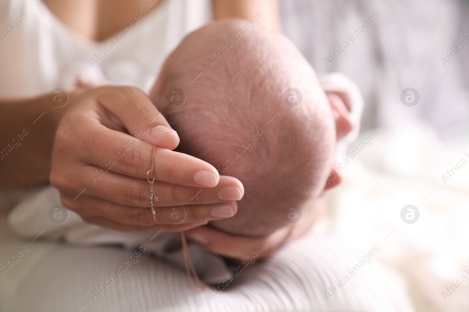 Photo of Mother holding newborn baby and Christian cross indoors, focus on hand