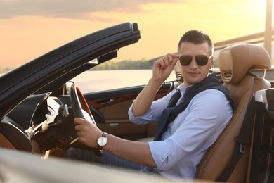 Stylish man driving modern luxury convertible car outdoors