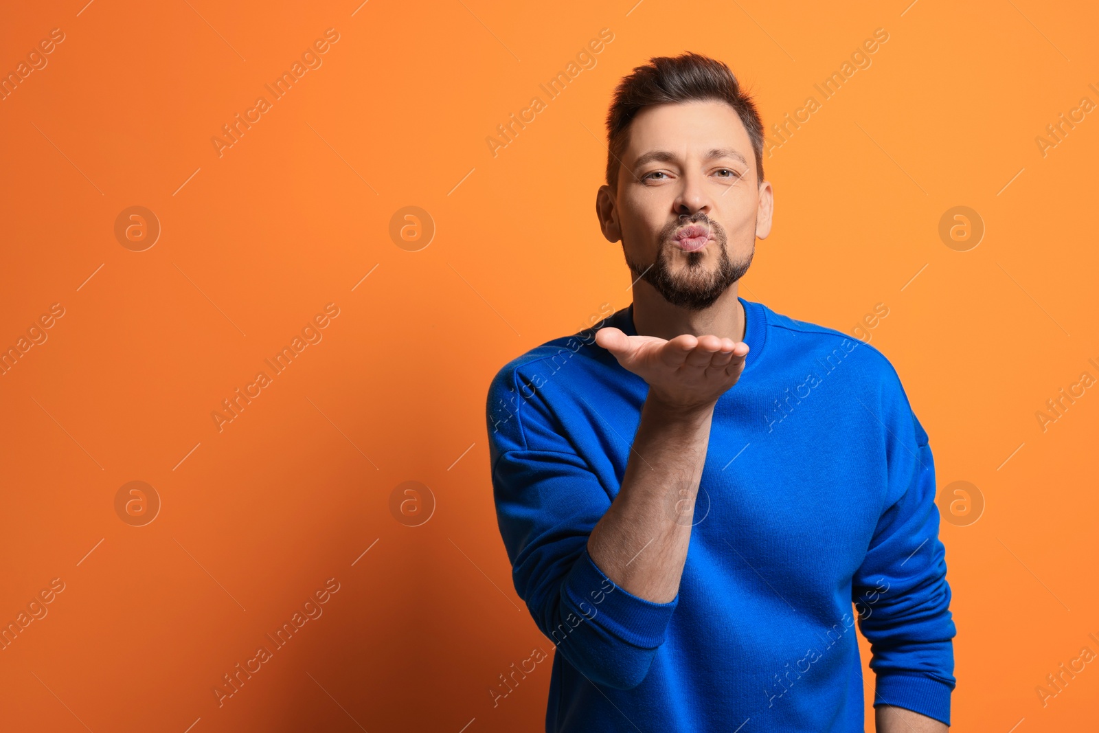 Photo of Handsome man blowing kiss on orange background. Space for text