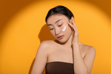 Photo of Beautiful young woman in sunlight with sun protection cream on her face against orange background