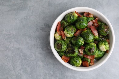 Delicious roasted Brussels sprouts and bacon in bowl on grey table, top view. Space for text