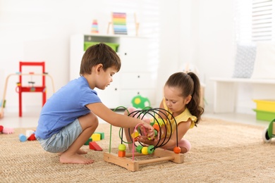Photo of Cute little children playing with bead maze on floor at home. Educational toy