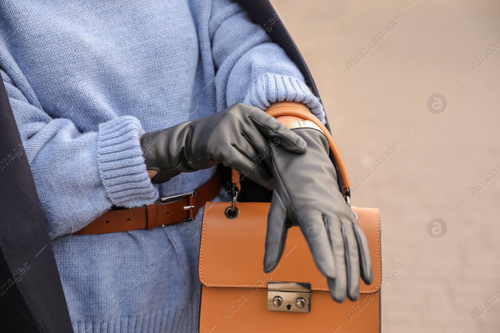 Photo of Young woman putting on stylish black leather gloves outdoors, closeup