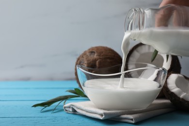 Photo of Woman pouring delicious coconut milk into bowl on light blue wooden table, closeup. Space for text