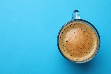Fresh coffee in cup on light blue background, top view. Space for text