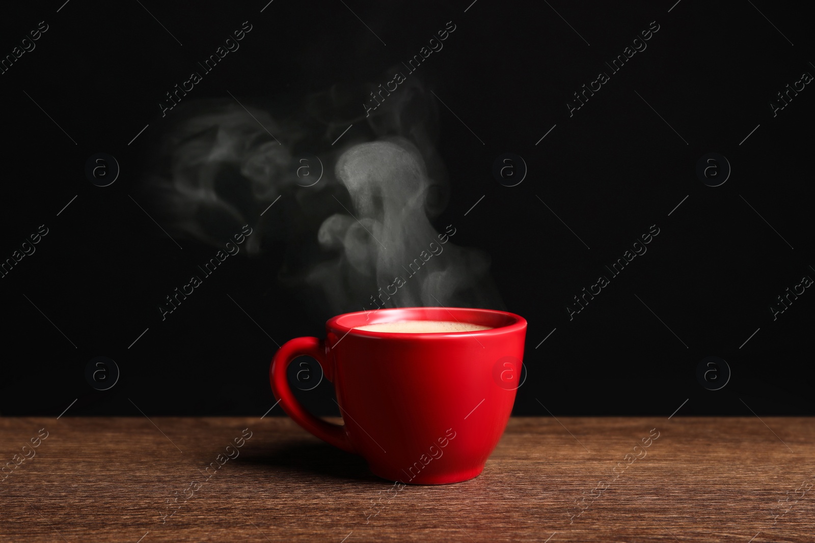 Image of Red cup with hot steaming coffee on wooden table against black background