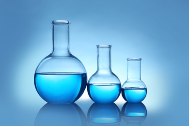 Photo of Flasks with liquid on table against color background. Laboratory analysis