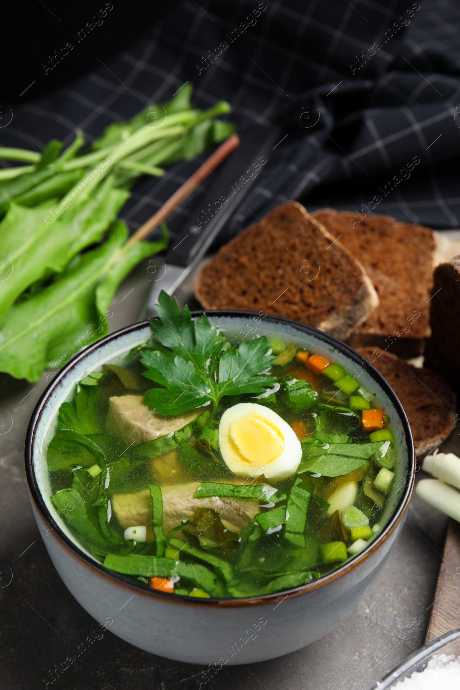 Photo of Delicious sorrel soup with meat and egg served on grey table