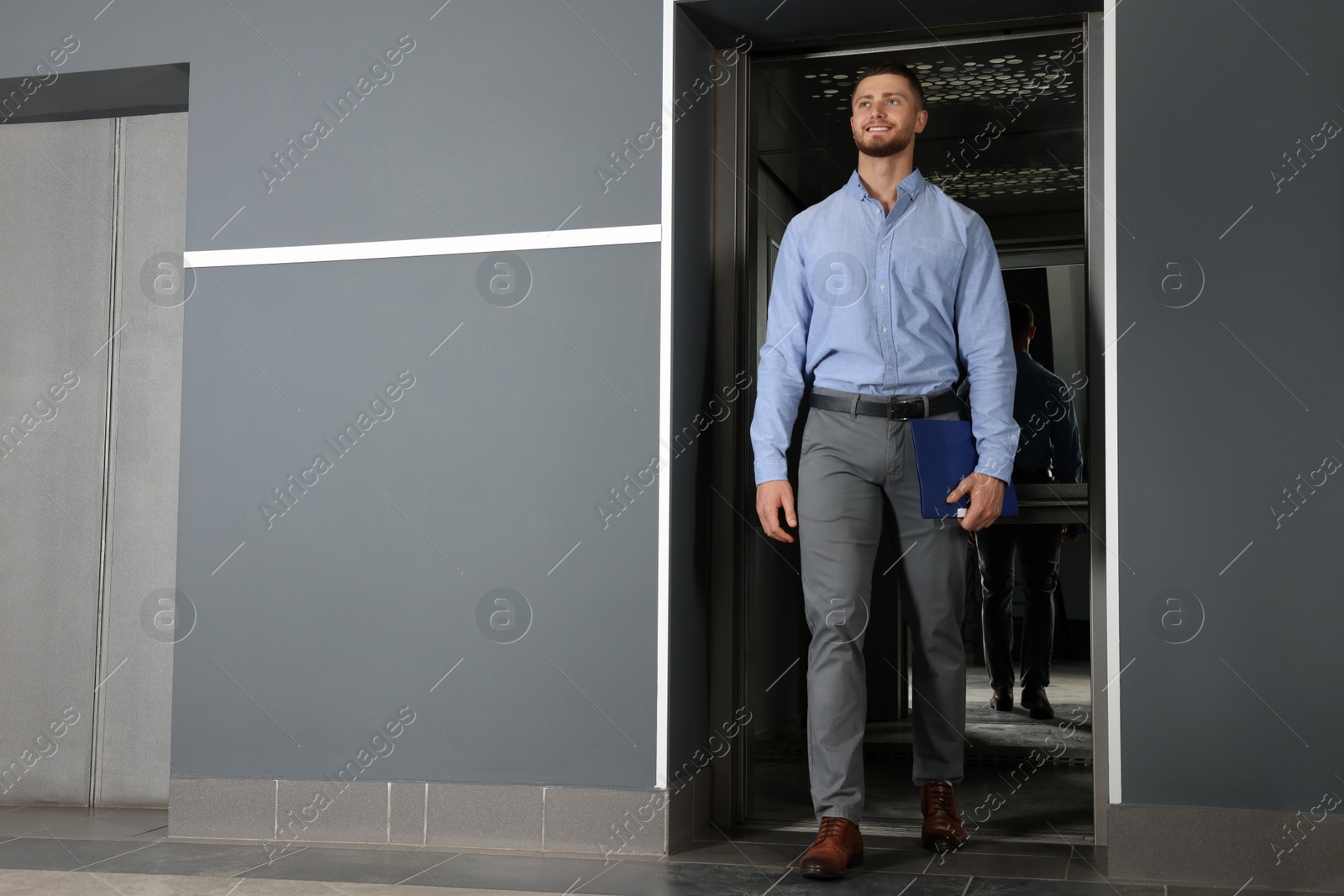 Photo of Attractive young businessman walking out modern elevator