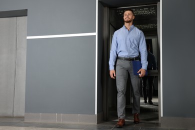 Photo of Attractive young businessman walking out modern elevator
