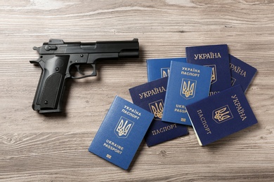 Photo of Gun with Ukrainian passports on wooden background, flat lay