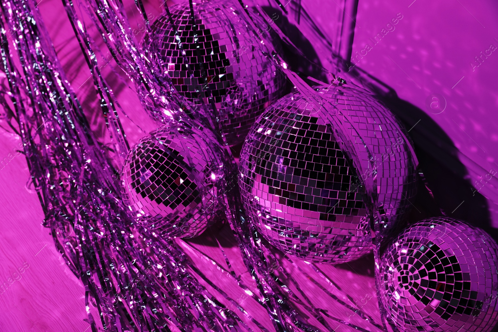 Photo of Shiny disco balls and foil fringe curtain indoors, toned in purple