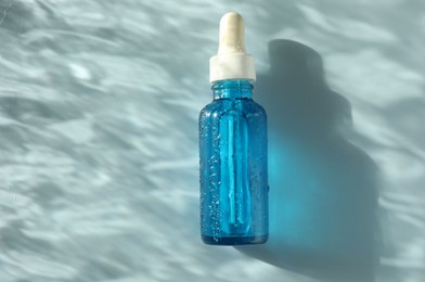 Wet bottle of cosmetic serum on light blue background, top view. Space for text