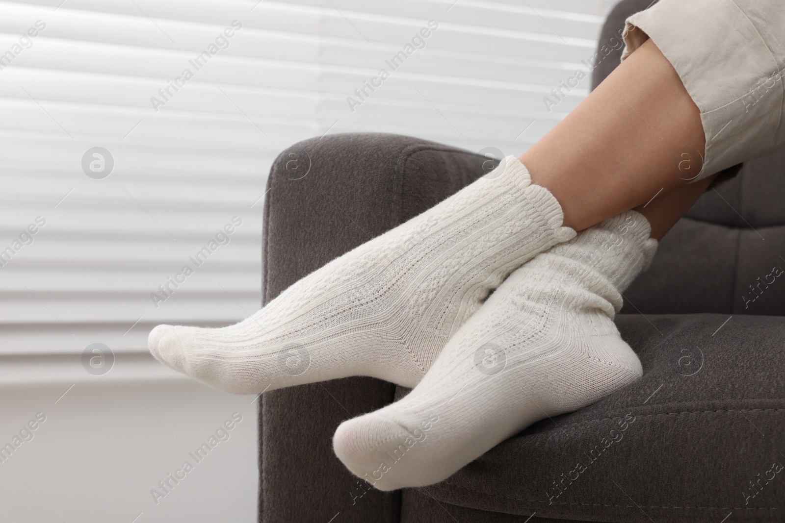 Photo of Woman in warm socks relaxing on armchair at home, closeup. Space for text