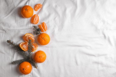 Photo of Delicious ripe tangerines and fir branches on white bedsheet, flat lay. Space for text