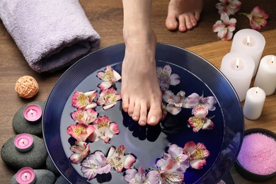 Woman holding her foot over bowl with water and flowers on wooden floor, closeup. Spa treatment