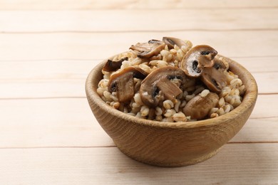 Delicious pearl barley with mushrooms in bowl on wooden table, closeup. Space for text