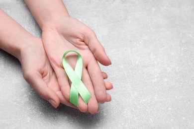 Photo of World Mental Health Day. Woman holding green ribbon on light grey background, closeup with space for text